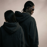 Two people wearing black hoodies with text on a plain background